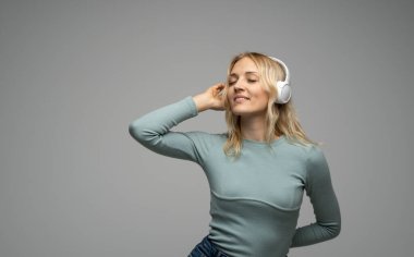 Güzel dans eden genç bir kadın koyu gri arka planda kablosuz kulaklıkla müzik dinliyor..