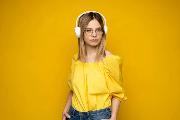 Menina muito jovem em camiseta amarela ouvir música com fones de ouvido e posando isolado no fundo da parede amarela. Pessoas emoções conceito de estilo de vida. Mock up espaço de cópia. — Fotografia de Stock