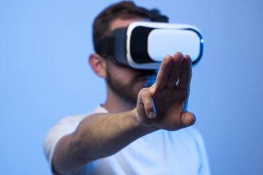Şaşırmış genç sakallı adam, yüksek teknoloji ürünü VR gözlükler takıyor, 360 derecelik video izliyor ya da metaevrende video oyunu oynuyor.