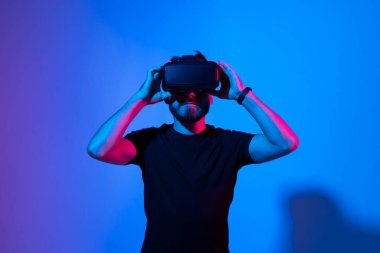 Şaşırmış genç sakallı adam, yüksek teknoloji ürünü VR gözlükler takıyor, 360 derecelik video izliyor ya da metaevrende video oyunu oynuyor.