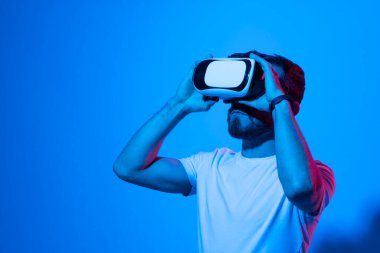 Modern stüdyoda neon ışığı olan sanal gerçeklik gözlüğü takan genç bir adamın yakın çekimi. Smartphone, VR kulaklığı kullanıyor. Gelecekteki teknoloji konsepti