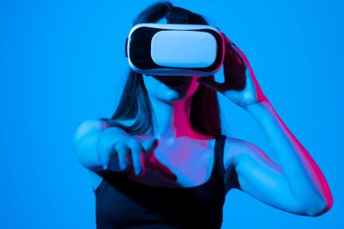 Gri arka planda VR gözlükleri takan genç bir kadın. Modern mimar iş yerinde sanal gerçeklik gözlüğü kullanıyor. Artırılmış gerçeklik vr stüdyosunda çalışan tasarımcı