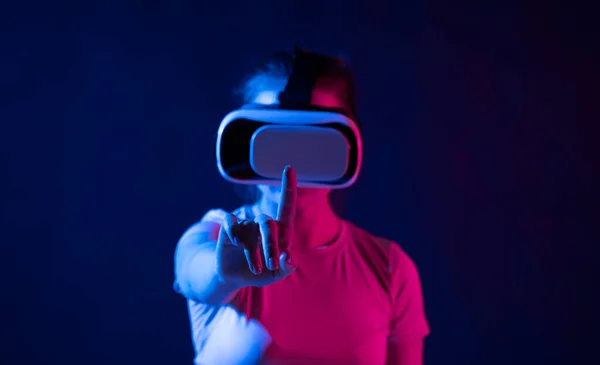 Metaverse technology concept. Woman with VR virtual reality goggles trying to touch something with a finger. Futuristic lifestyle