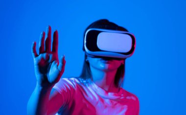Gri arka planda VR gözlükleri takan genç bir kadın. Modern mimar iş yerinde sanal gerçeklik gözlüğü kullanıyor. Artırılmış gerçeklik vr stüdyosunda çalışan tasarımcı