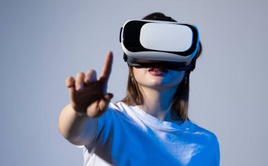 Gri arka planda VR gözlükleri takan genç bir kadın. Modern mimar iş yerinde sanal gerçeklik gözlüğü kullanıyor. Artırılmış gerçeklik vr stüdyosunda çalışan tasarımcı