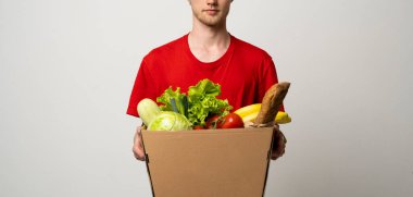 Kırmızı üniformalı kurye marketten taze yiyecek paketi taşıyor. Teslimat konsepti