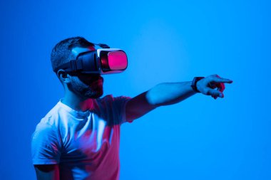 Sanal dünyada metaçağ teknolojisi yeniliklerini kullanarak beyaz tişörtlü bir adam VR gözlük takıyor. AR kavramı neon ışıkları ve karanlık arka plan üzerinde. Sanal gerçeklik deneyimi. Gelecek teknolojisi