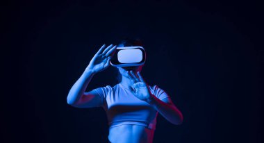 Young woman wearing vr headset and watching 360 videos in neon light. Girl toching virtual objects in vr glasses