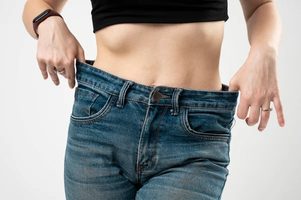 白い背景に減量の結果を示す青いジーンズのスリムスポーティな女性 ダイエットの概念と減量 — ストック写真