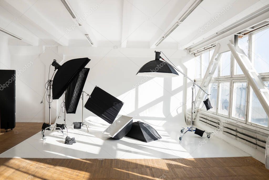 Professional lighting equipment, flashes, c-stands on a cyclorama in modern photo studio with a huge windows. Octabox, stripbox, softbox, buety plate and other stuff for photography