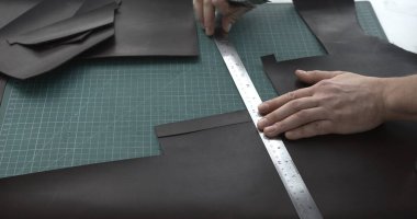 Üst düzey deri ustası, kahverengi deri işiyle uğraşıyor. Bıçak, metal cetvel ve kahverengi deriyi parçalara ayırıyor. El yapımı konsept.