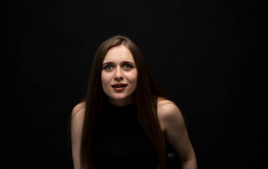 Siyah bir odada siyah tişörtlü, uzun saçlı, üzgün, esmer bir kızın portresi. Kızgın ve üzgün duygular.