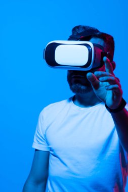 VR kulaklıklı yakışıklı genç adam işaret ediyor ve gördüğü bir şeye dokunmaya çalışıyor. Sanal gerçeklik kavramı