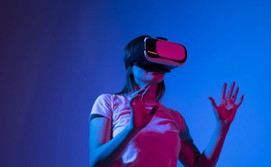 Young woman wearing VR headset while working with engineering project in lab with three dimensional printing in neon light studio. High tech engineering concept