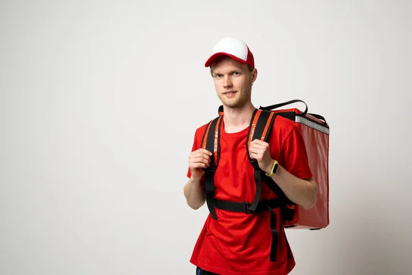 Delivery man in a red uniform carry thermal backpack full of food, groceries to the clients. Food delivery service