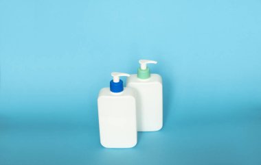 White cosmetic plastic bottles with black pump dispenser on blue background. Liquid containers for gel, lotion, cream, shampoo, bath foam