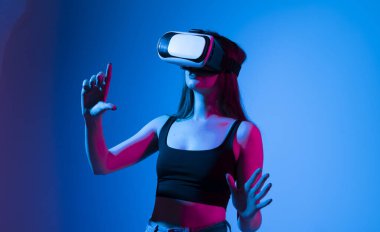 Virtual reality concept. Young brunette woman wearing a VR headset and looking up while playing a game with a friends in a metaverse