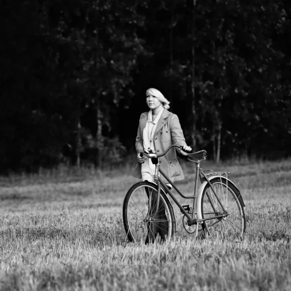 Jovem menina bonita andando em um campo com uma bicicleta — Fotografia de Stock