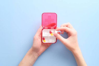 Mavi arka planda hapları olan ilk yardım çantası taşıyan bir kadın. Tıbbi konsept.