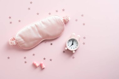 Uyku maskesi, kulak tıkaçları, pastel pembe arka planda çalar saat. Uykusuzluk tedavisi için. Düz yatış, üst görünüm