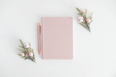 Kalemli pembe defter ve beyaz arka planda pembe toplarla süslenmiş Noel ağacı dalları. Zarif Noel kadınsı çalışma alanı üst görünümü.