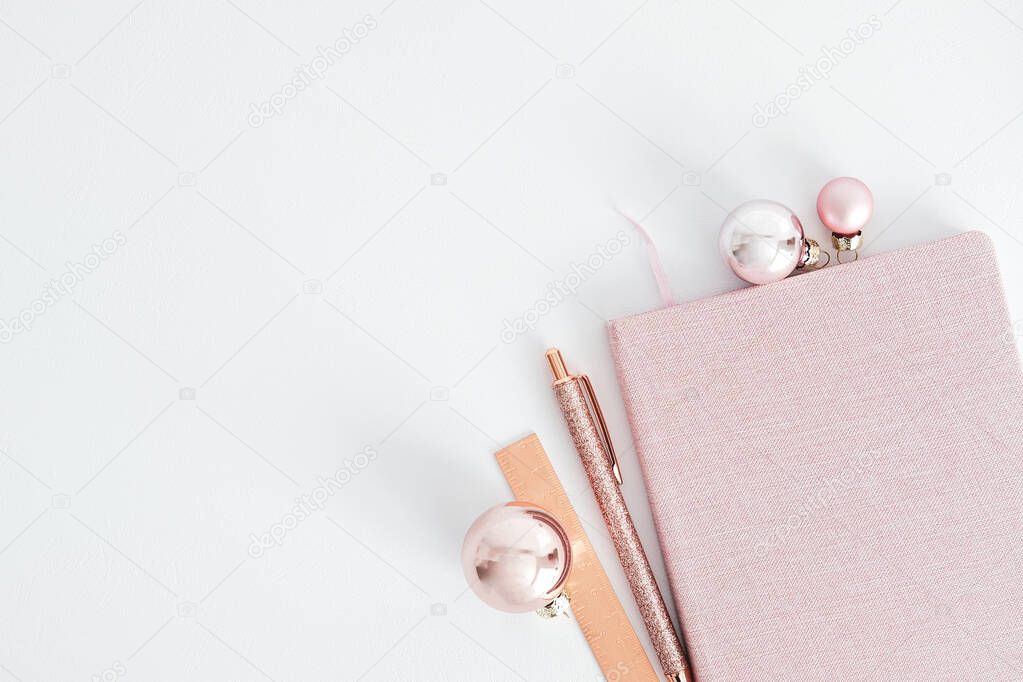 Christmas holiday festive workspace top view. Glamour pink notebook, balls and office accessories on white background. Top view with copy space. Minimal style.