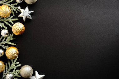 Altın ve gümüş Noel süslemeleri ve yıldız süslemeleri. Siyah arka planda köknar dalları ve fotokopi alanı. Mutlu Noeller ve mutlu yıllar tebrik kartı. Asgari düzeyde. Düz yatış, üst görünüm.