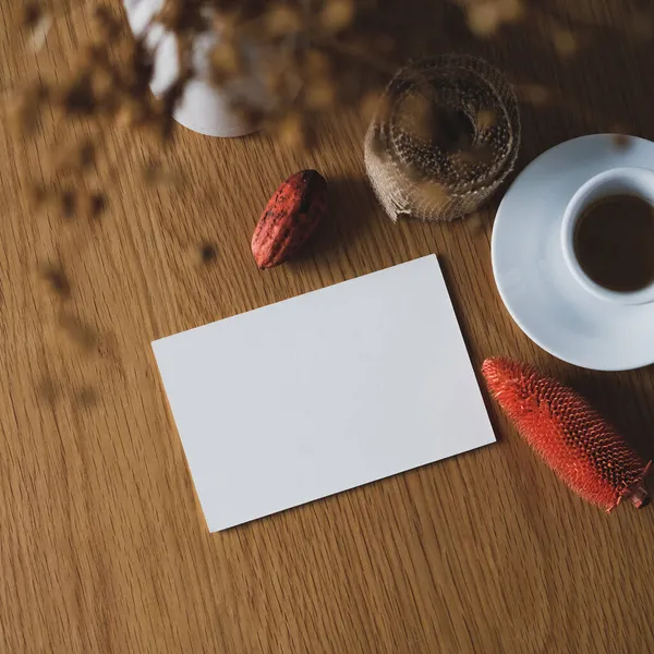Sonbahar durgun bir hayattır. Kağıt kart maketi, bir fincan kahve, sonbahar süsü, ahşap masada kurumuş çiçek vazosu..