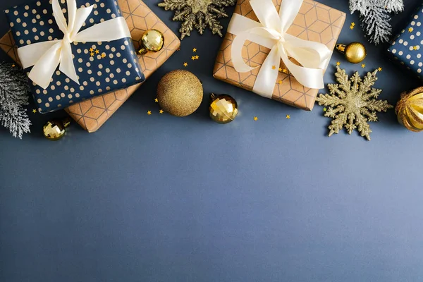 Christmas frame top border made of Xmas gift boxes, gold baubles , snowflakes on dark blue background. Flat lay, top view, copy space. Elegant Christmas card design.