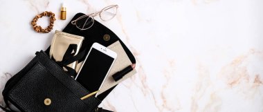 Akıllı telefon, çanta, kağıt defter, ruj, kadın gözlüğü, bilye masasında saç tokası olan siyah deri kadın çantası. Güzellik blogu afişi tasarımı. Düz konum, üst görünüm, kopyalama alanı.