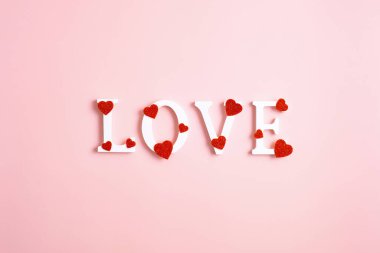 Aşk kelimesi pembe arka planda kırmızı kalplerle süslenmiş. Sevgililer Günün kutlu olsun. Düz yatış, üst görünüm