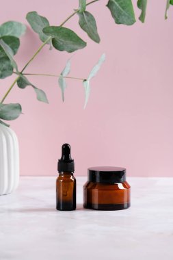 Kehribar cam damlası şişesi ve pembe arka planda bir kavanoz krema. Kozmetik ürünleri markalaşma modeli.