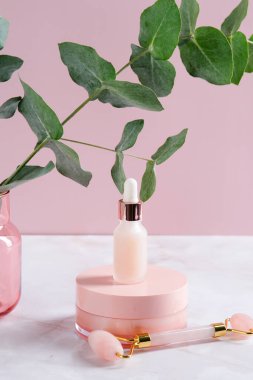 Pembe kozmetik kaplar ve okaliptüslü yüz masajı silindiri. Yüz bakımı konsepti. Güzellik ürünleri ambalaj tasarımı