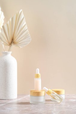 Temel yağlı kozmetik şişeler, vücut kremi ve bej arka planda kuru çiçek vazosu..