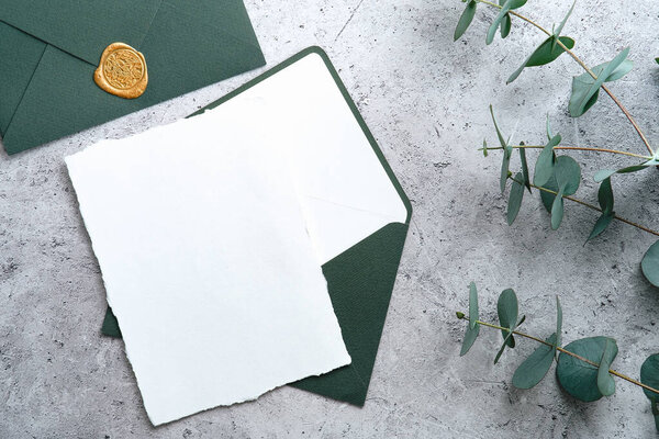 Wedding stationery set. Wedding invitation card template, green envelope, eucalyptus branches on concrete background. Flat lay, top view, copy space.