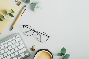 Düz masa masası, gözlüklü, bilgisayar klavyeli kağıt defter, kalem, okaliptüs dallı. Zarif kadınsı çalışma alanı, yukarıdan görünüm.