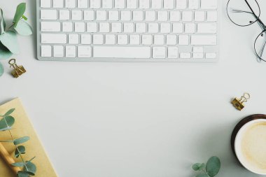 Ofis masasında klavye, kahve fincanı, okaliptüs dalları ve ofis malzemeleri. Zarif kadın çalışma alanı üst görüşü. Düz uzanın, başınızın üstünde.