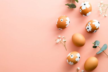 Zarif Paskalya kompozisyonu. Pastel pembe masada renkli Paskalya yumurtaları ve çiçekler. Mutlu Paskalyalar. Asgari biçim.