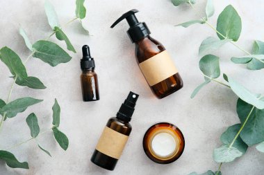 Okaliptüs dallı doğal cilt bakım ürünleri, taş masa, üst görünüm. Amber cam kozmetik ambalaj tasarımı, güzellik ürünleri markalaşma.