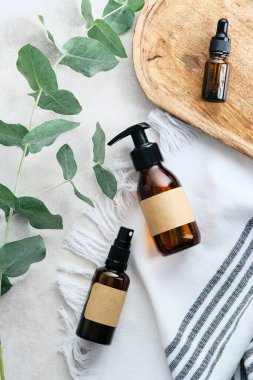 SPA doğal organik kozmetik seti banyo manzaralı masada. Boş etiketli ve okaliptüs dallı Amber cam kaplar.