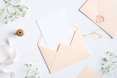 İçinde düğün davetiyesi olan zarf mermer masanın üzerinde. Düğün kırtasiye seti. Düz konum, üst görünüm, kopyalama alanı.