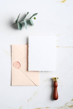 Düğün davetiyesi maketi, zarf, balmumu mühür, mermer masanın üzerindeki okaliptüs dalı. Düğün kırtasiye seti. Düz yatış, üst görünüm.