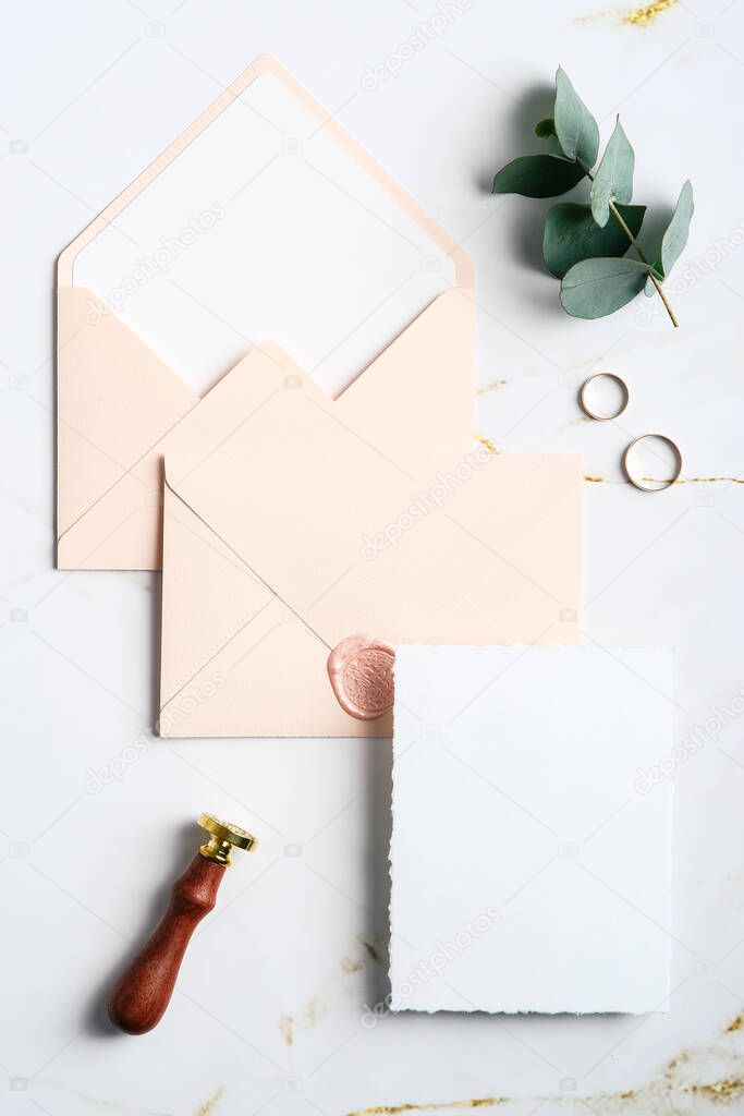 Elegant wedding stationery set. Wedding invitation card template, pastel pink envelopes, wax seal stamp, rings, eucalyptus on marble table. Flat lay, top view, copy space.