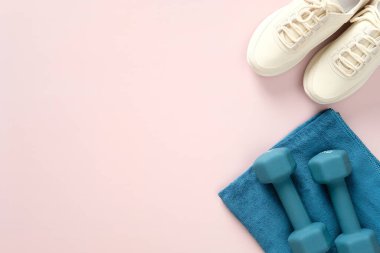 Spor ayakkabı, havlu ve pastel pembe arka planda dambıllar. Fitness, egzersiz, sağlıklı yaşam tarzı konsepti. Düz konum, üst görünüm, kopyalama alanı. Spor blog afişi tasarımı.