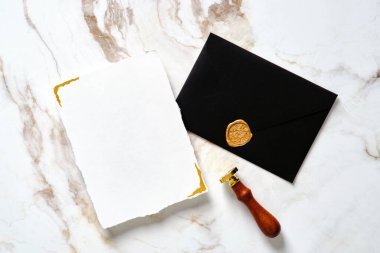 Lüks düğün kırtasiye seti. Düğün davetiyesi maketi, siyah düğün zarfı, altın mermer masa üzerindeki balmumu mühür..