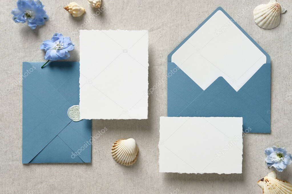 Wedding stationery set. Nautical wedding invitation cards mockups and blue envelopes with seashell and flowers on beige background. Top view, flat lay, copy space.