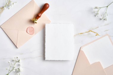 Düğün kırtasiyesi mermer masa manzaralı. Boş kağıt maketi, üzerinde balmumu mühür olan pastel pembe zarflar, çigila çiçekleri..