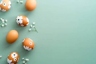 Mutlu Paskalya kartı tasarımları. Pastel yeşil arka planda çiçeklerle süslenmiş Paskalya yumurtaları. Düz yatış, üst görünüm.