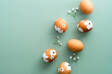 Zarif Paskalya bezi. Paskalya yumurtaları pastel yeşil arka planda bahar çiçeklerini süsledi. Düz yatış, üst görünüm