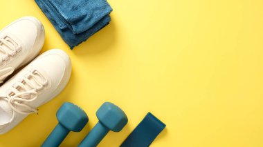 Sarı arka planda spor yapmak için spor aletleri, üst manzara. Düz yatıyordu kadın spor ayakkabıları, havlu, halterler, fitness bandı.